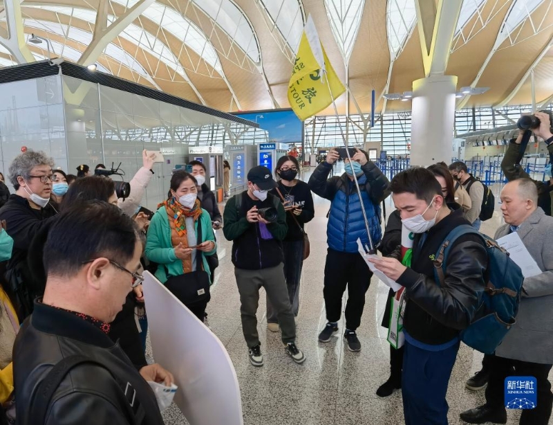 2月6日，在上海浦東國際機(jī)場，出境團(tuán)隊(duì)游領(lǐng)隊(duì)師文（舉旗者）向游客說明相關(guān)注意事項(xiàng)。（圖源：新華社）